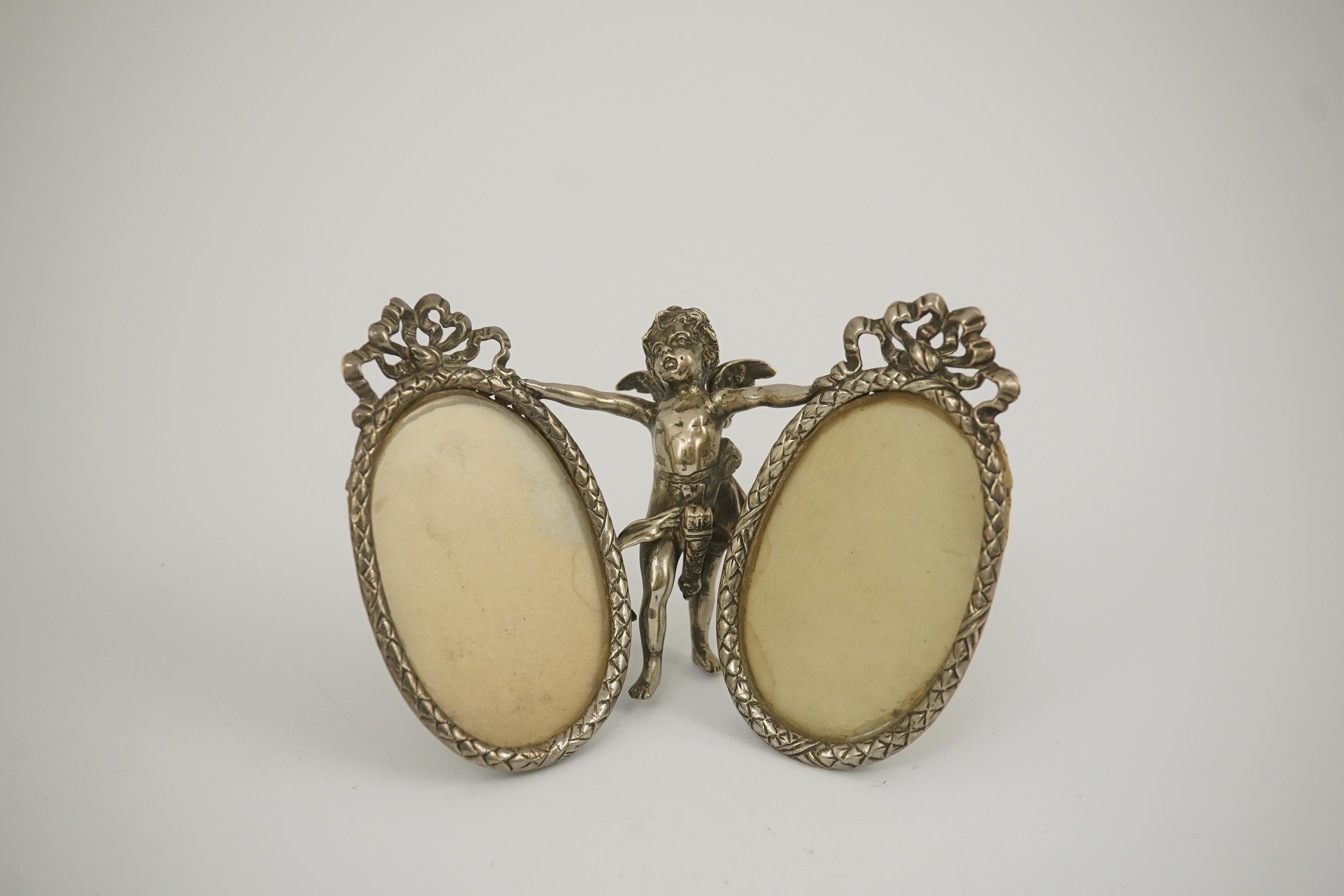 A late 19th century Hanau silver double oval photograph frame, supported by central figure of Cupid, by Berthold Muller